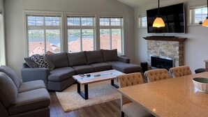 A modern living room with a sectional sofa, a coffee table, a fireplace, and a TV mounted above it. - Lake and Mountain Views | Golf cart | Boat slip (Osoyoos)