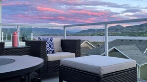 A balcony with wicker furniture, a table, and a view of a lake and mountains. - Lake and Mountain Views | Golf cart | Boat slip (Osoyoos)