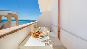 A balcony with a table set for two, featuring a bottle, glasses, and a plate of food. A clear view of the sea and a building with arches is visible in the background. - Residence Bellavista - App 4 PP (Torre Lapillo)