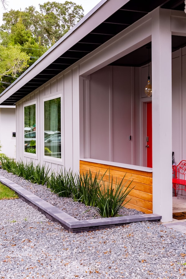 Une maison moderne dotée d’un porche abrité, d’une porte rouge et d’un chemin de gravier menant à l’entrée.