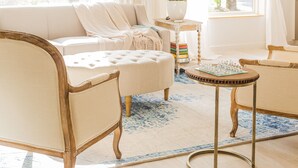 Een goed verlichte woonkamer met een bank, fauteuils, een bijzettafeltje met een schaakbord en een bloevas.