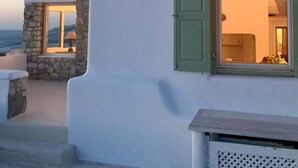 A white building with a stone window and a green shutter, overlooking a body of water. - Villa Ramona in Mykonos (Mykonos)