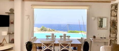 A dining area with a view of the sea, a stone wall, and a white sofa.