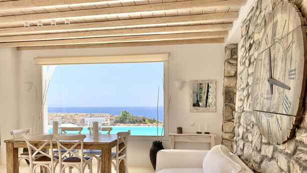 A spacious living area with a view of the sea, a stone wall, and a wooden ceiling. - Villa Ramona in Mykonos (Mykonos)