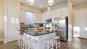 Uma cozinha moderna com armários brancos, eletrodomésticos de aço inoxidável e uma ilha central com banquetas.