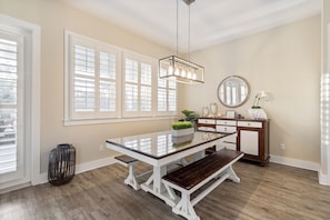 Un coin repas avec une table à plateau de verre, des bancs en bois, un luminaire suspendu, un miroir et une plante posée sur un meuble en bois.