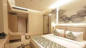 Una habitación de hotel moderna con una cama grande, una zona de estar con una silla y un banco, un espejo y una pared con un diseño decorativo.
