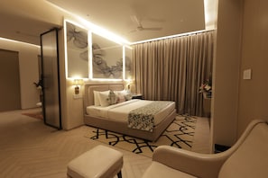A modern hotel room with a large bed, a sitting area, a ceiling fan, and a mirror. - Chinmay Hotels and Resorts (Lucknow)