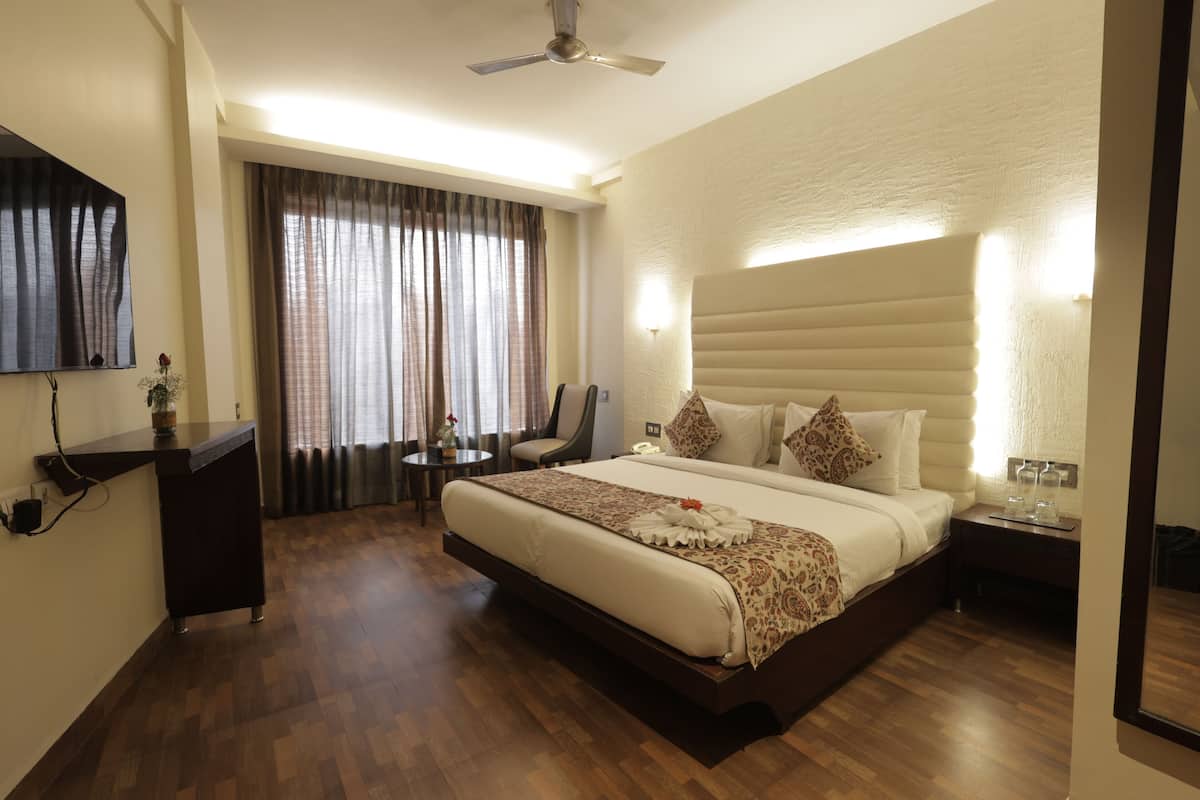 A hotel room with a large bed, a desk, a chair, a TV, and a ceiling fan.