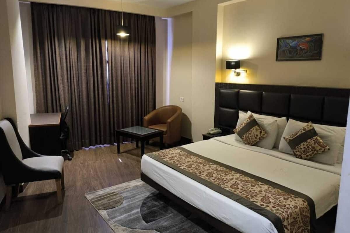 A hotel room with a bed, a desk, a chair, a lamp, and a painting on the wall.
