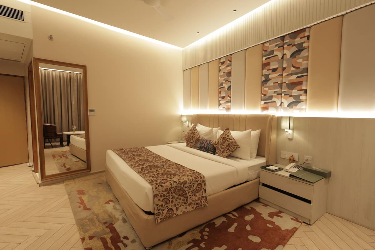A modern hotel room with a large bed, bedside tables, a mirror, and a patterned rug.