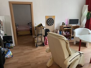 A room with a bed, a desk, a chair, a dartboard, and a television.