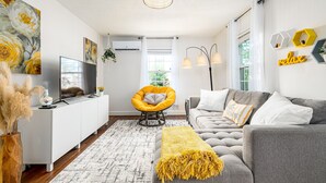 Un salon moderne avec un canapé gris, un fauteuil jaune et un meuble de rangement blanc pour les appareils électroniques.