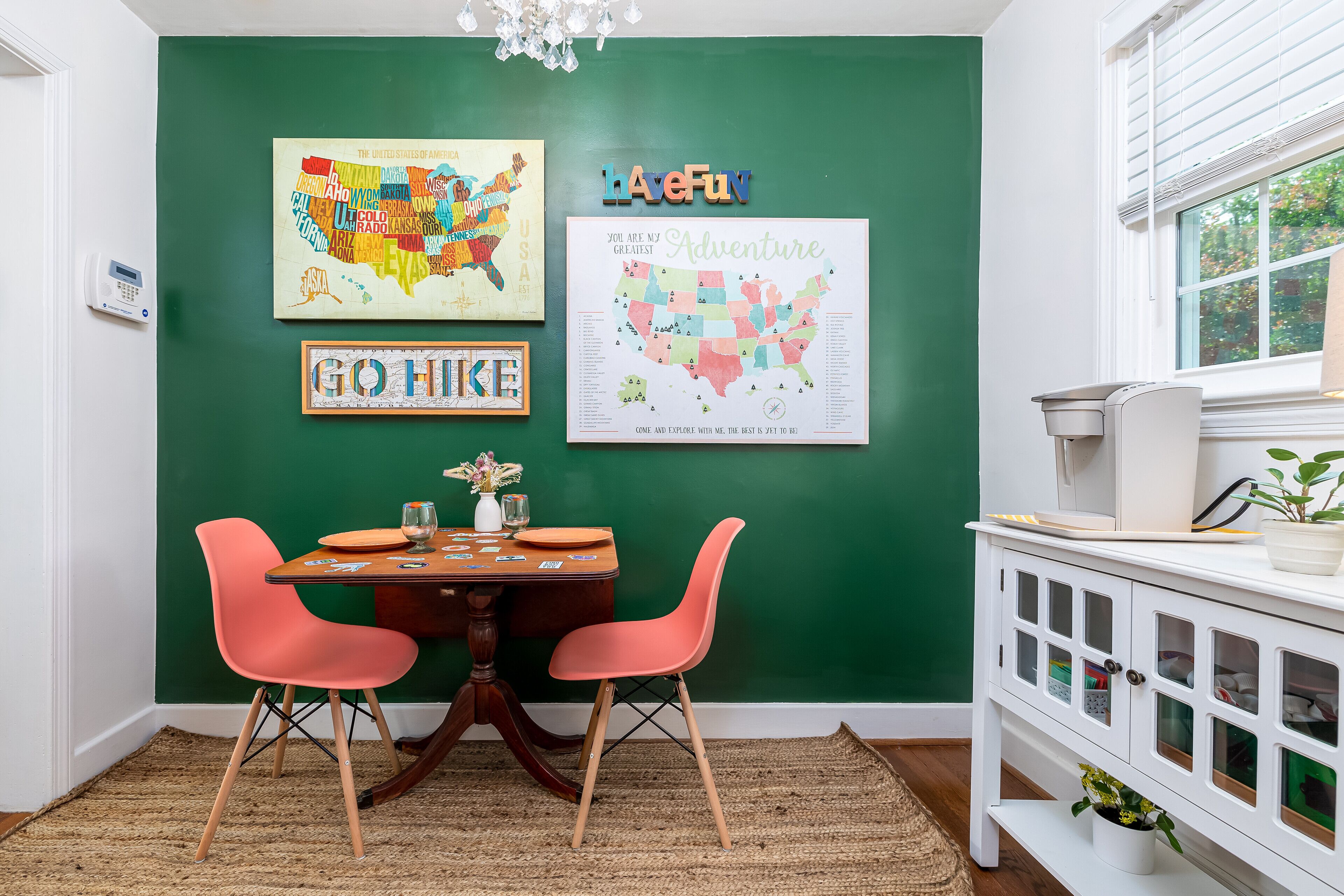 Un comedor con pared verde, dos sillas rosa, una mesa de madera y un armario blanco con puertas de cristal.