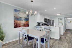 Una cocina moderna con armarios blancos, una isla central y un comedor con mesa y sillas.