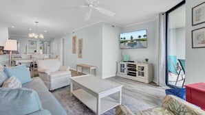 A modern living room with a sofa, a coffee table, a TV, and a dining area with chairs and a table. - Award-Winning Resort Amenities | Shipwatch 210B (Isle of Palms)
