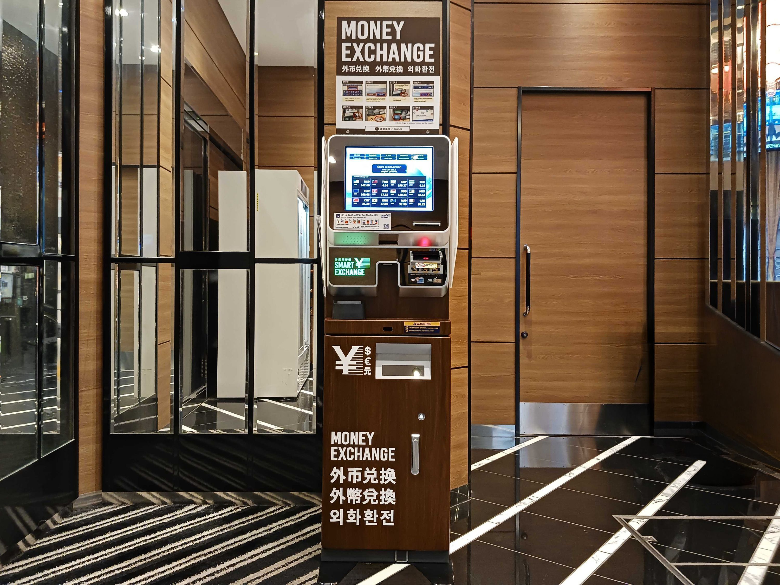 A money exchange machine with a digital interface, located in a modern lobby with wooden paneling and a reflective floor.