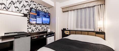 A hotel room with a bed, a desk, a TV mounted on the wall, and a window with curtains.