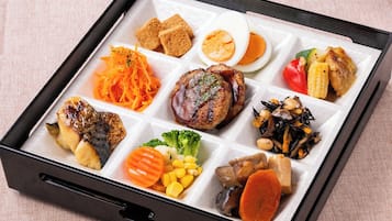 Un plateau-repas comprenant divers plats, notamment des escalopes panées, un œuf dur, de la viande grillée, des légumes et une portion de haricots.
