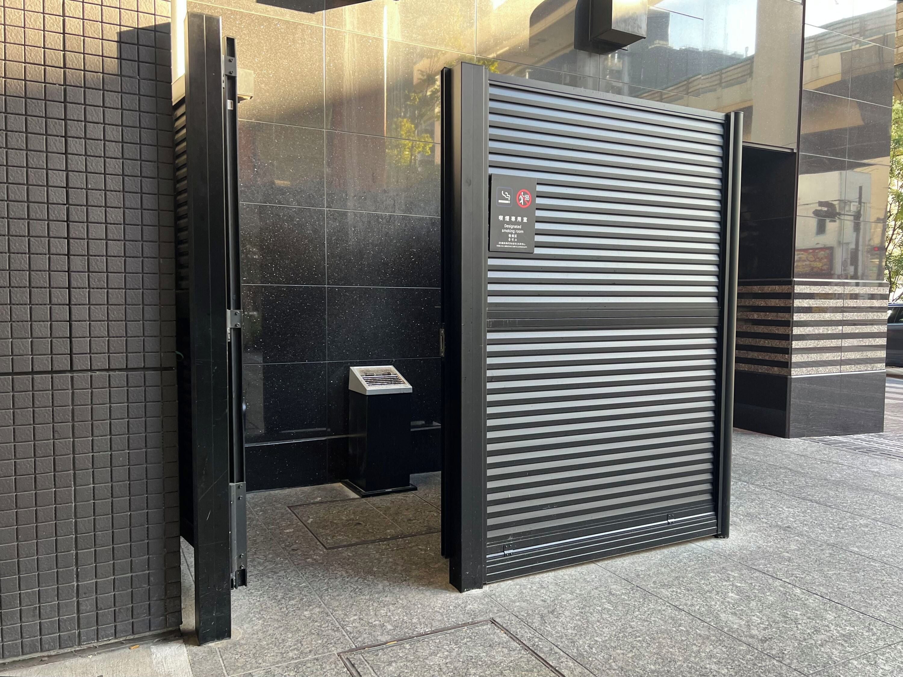 A closed metal gate with a no-smoking sign, a tiled wall, and a metal grate on the ground.