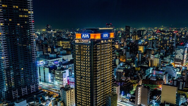 A high-rise building with APA signage, surrounded by a dense urban area with various other buildings and illuminated streets. - APA Hotel & Resort Osaka Umeda Eki Tower (Osaka)