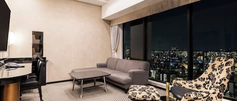 A modern hotel room with a city view, a sofa, a chair, a small table, and a desk with a telephone.