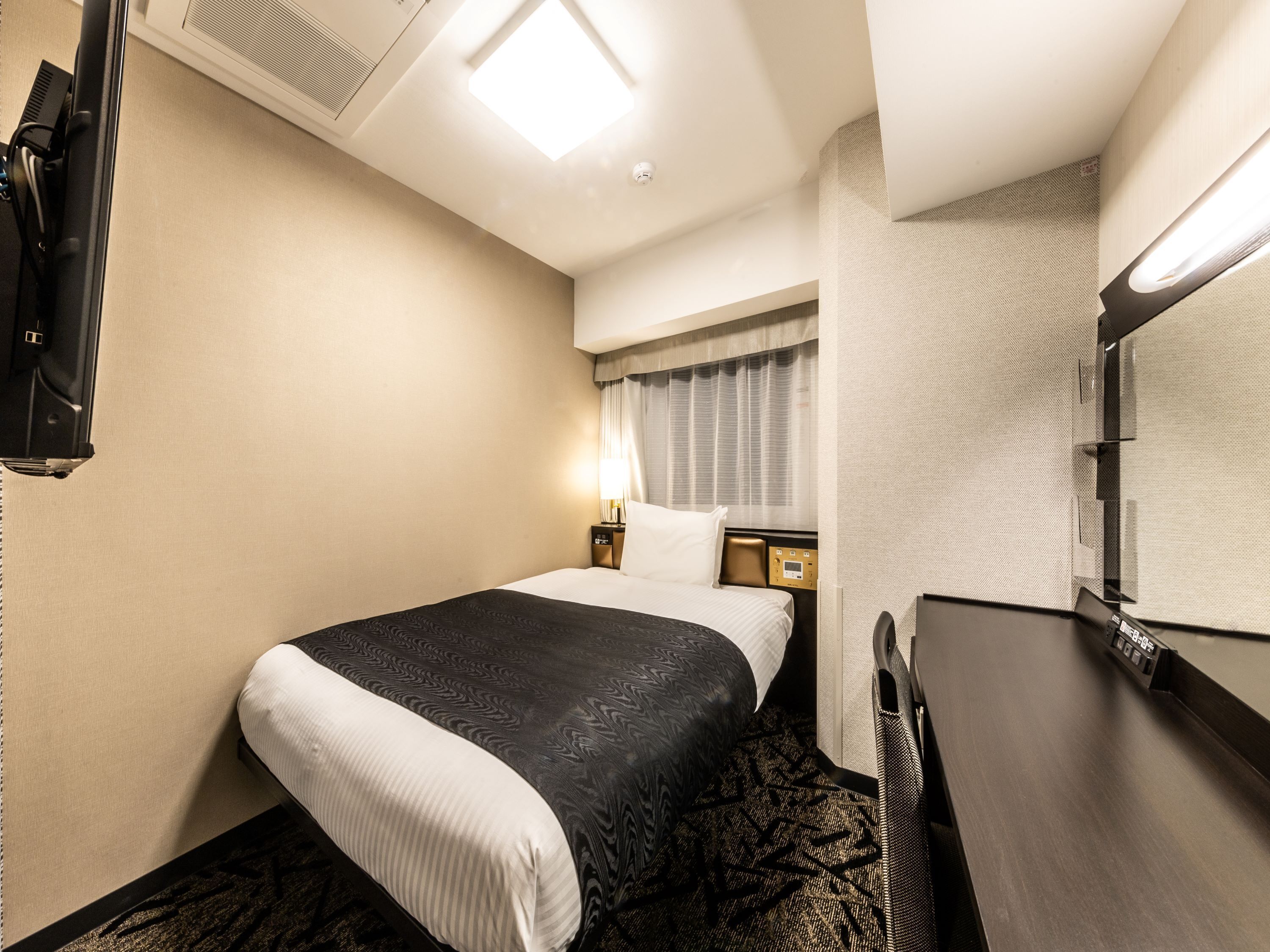A hotel room with a bed, a desk, a TV, and a window with curtains.