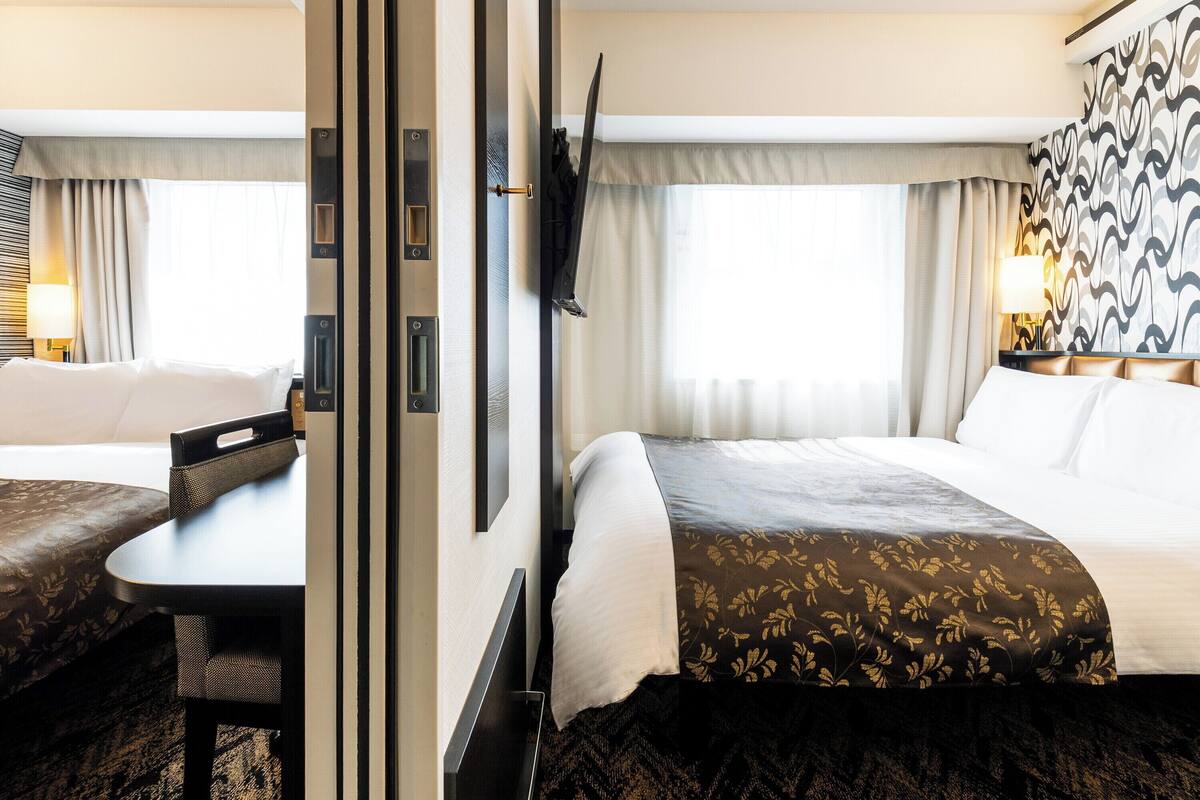 A hotel room with a bed, a desk, a chair, a TV mounted on the wall, and a patterned curtain.