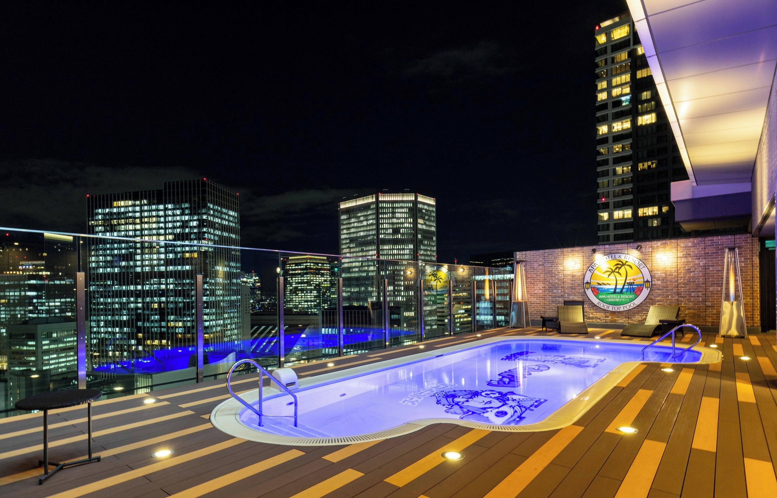 A rooftop pool with a cityscape view, a lounge area, and a sign for the APA Hotel & Resort.