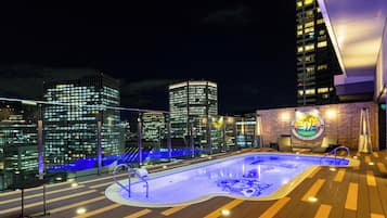 A rooftop pool with a cityscape view, a lounge area, and a sign for the APA Hotel & Resort.