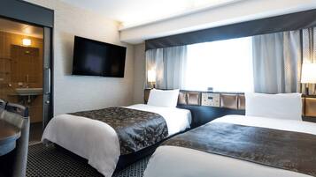 A hotel room with two beds, a TV mounted on the wall, a desk with a chair, and a window with curtains.
