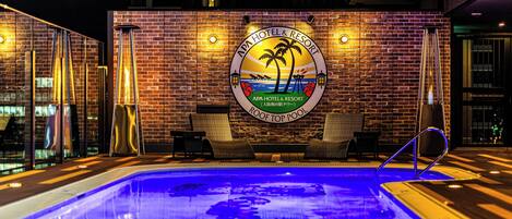 Une piscine située sur le toit, avec une enseigne indiquant «
APA Hotel & Resort
», et un logo représentant des palmiers et un coucher de soleil.