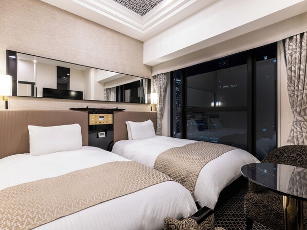 A hotel room with two beds, a large mirror, a control panel, a window with a city view, and a small table.