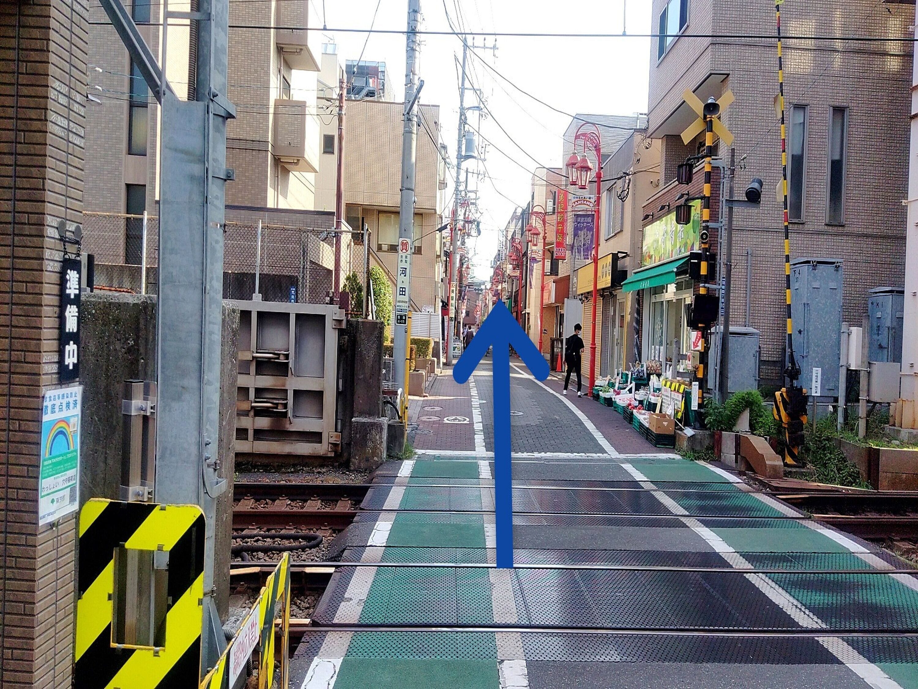 A train station platform with tracks, a blue directional arrow, and buildings on either side.