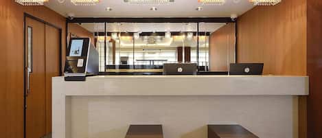 Een hotel receptie met een marmeren balie, twee HP laptops, een digitale kiosk en een kroonluchter.
