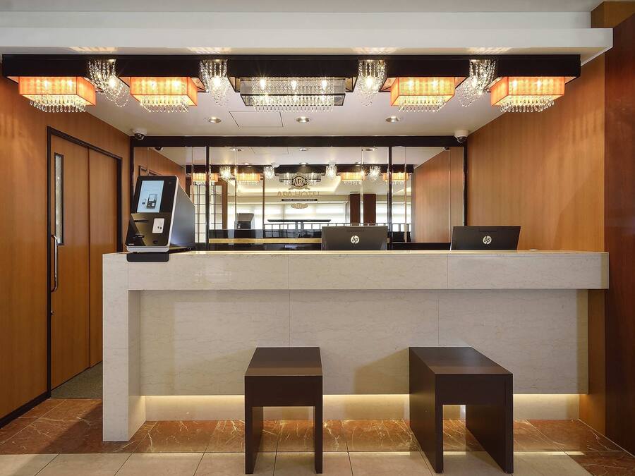 A hotel reception area with a marble counter, two HP laptops, a digital kiosk, and a chandelier.