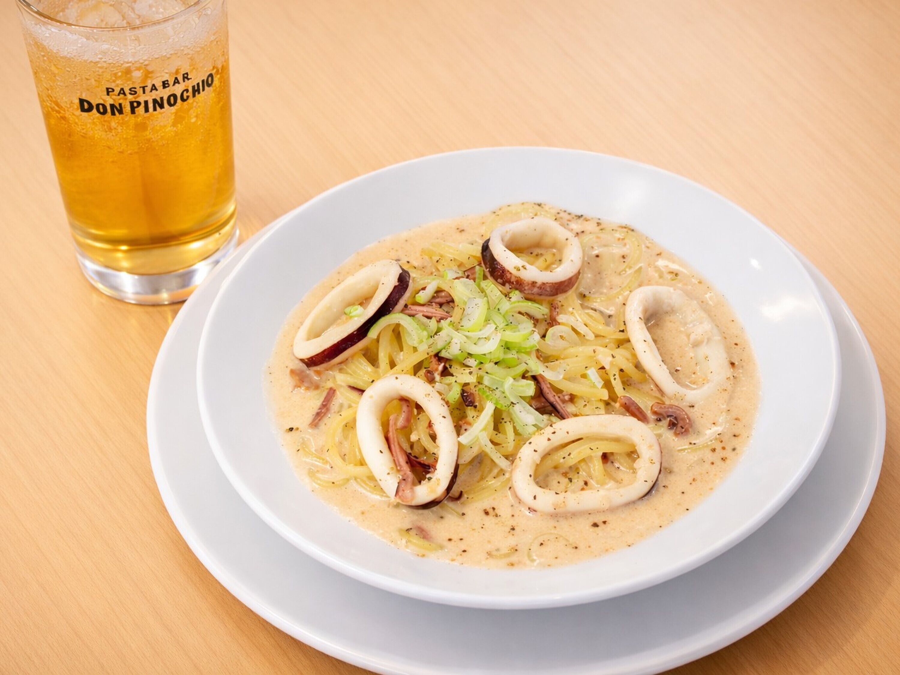 Une assiette de pâtes garnie d’anneaux de calamars et d’oignons verts, accompagnée d’un verre de bière.