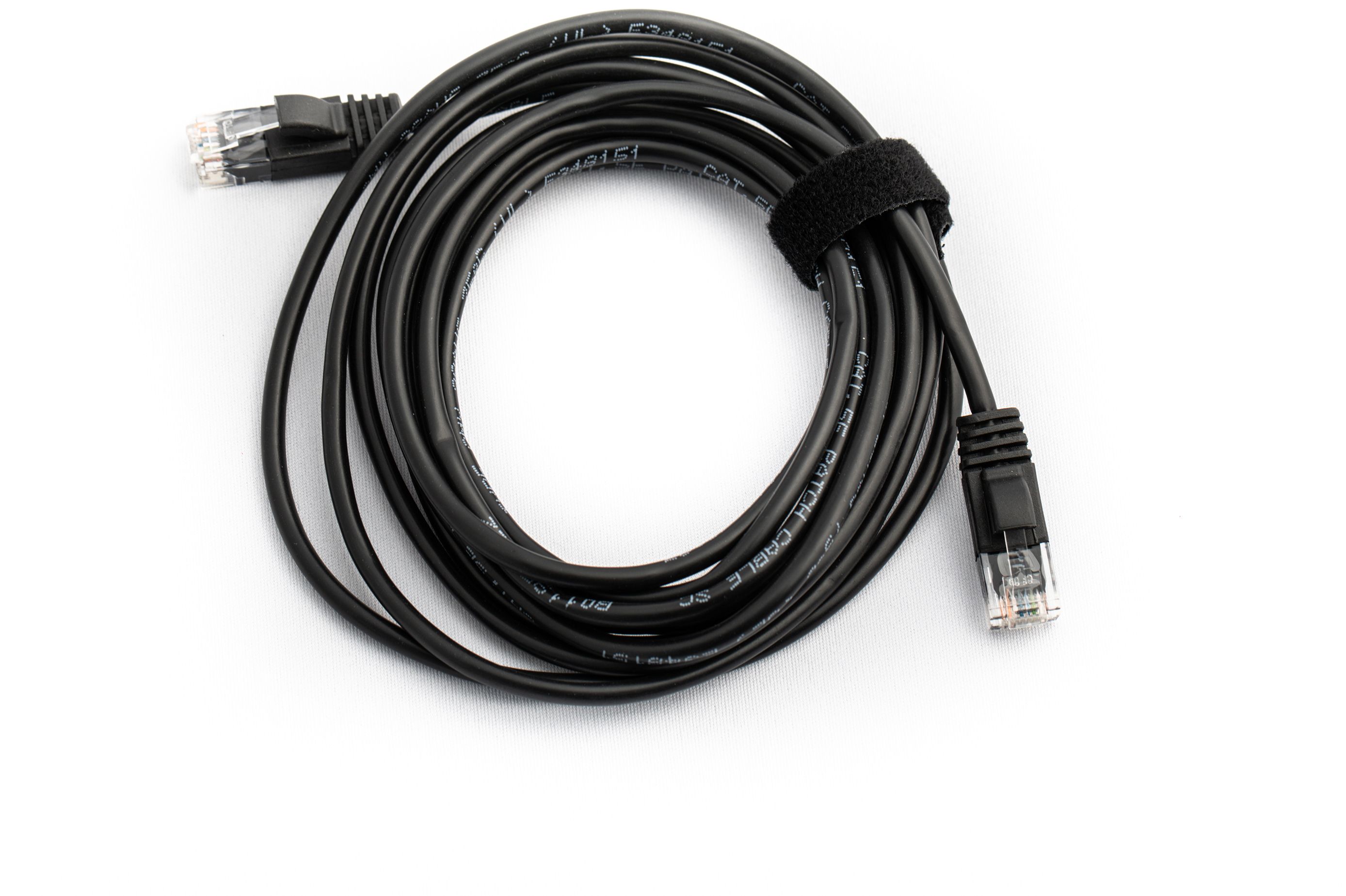 Een zwarte Ethernetkabel met RJ45 connectoren aan beide uiteinden, opgerold op een wit oppervlak.