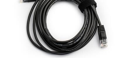 Cable Ethernet negro con conectores RJ45 en ambos extremos, enrollado sobre una superficie blanca.
