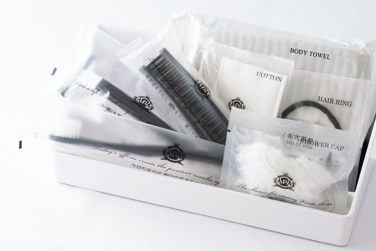 Caixa branca com uma toalha de banho, algodão, um prendedor de cabelo e touca de chuveiro.