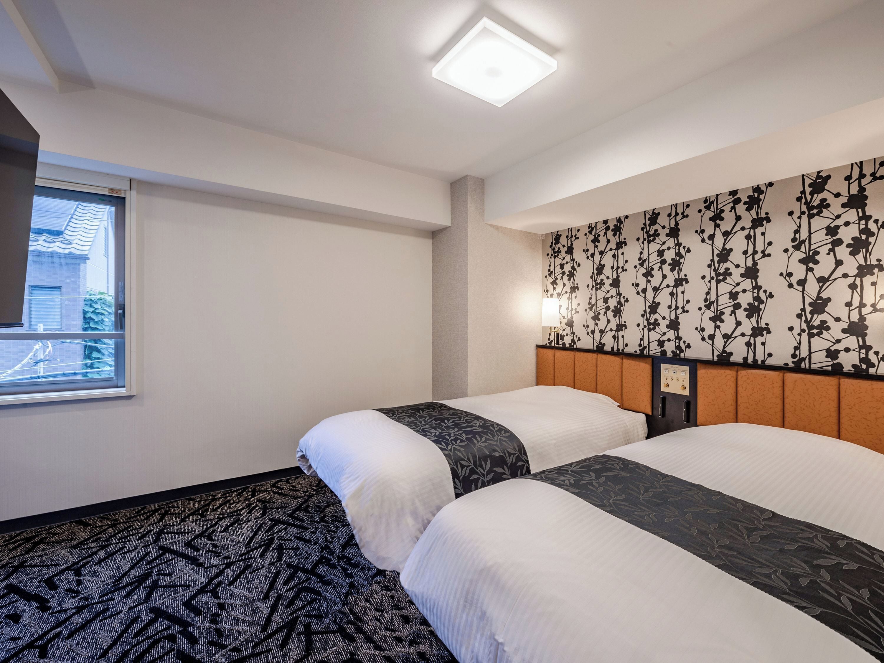 Une chambre d’hôtel avec deux lits, une fenêtre donnant sur un paysage agréable, un mur décoré d’un motif et un luminaire au plafond.