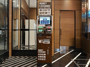 A money exchange machine with a digital interface, located in a modern lobby with wooden paneling and a reflective floor. - APA Hotel Asakusabashi Ekimae (Tokyo)