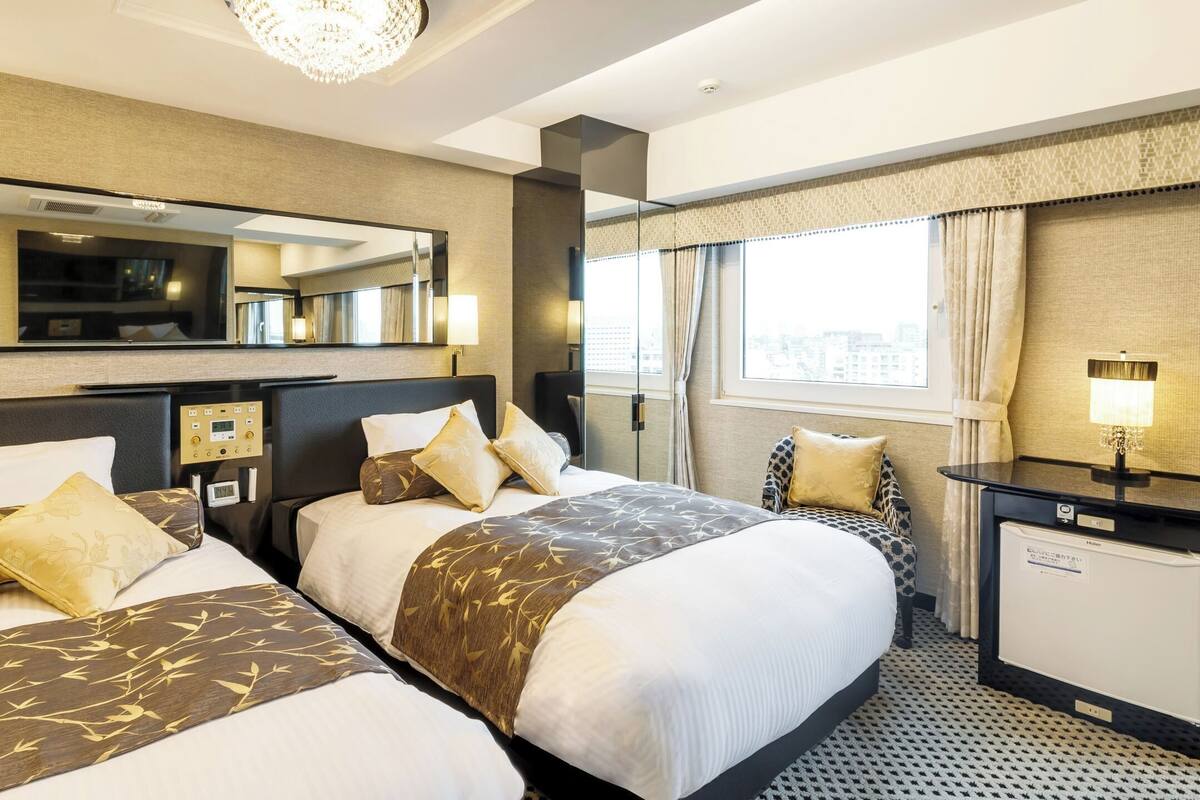 A hotel room with two beds, a TV, a control panel, a desk, and a window with curtains.