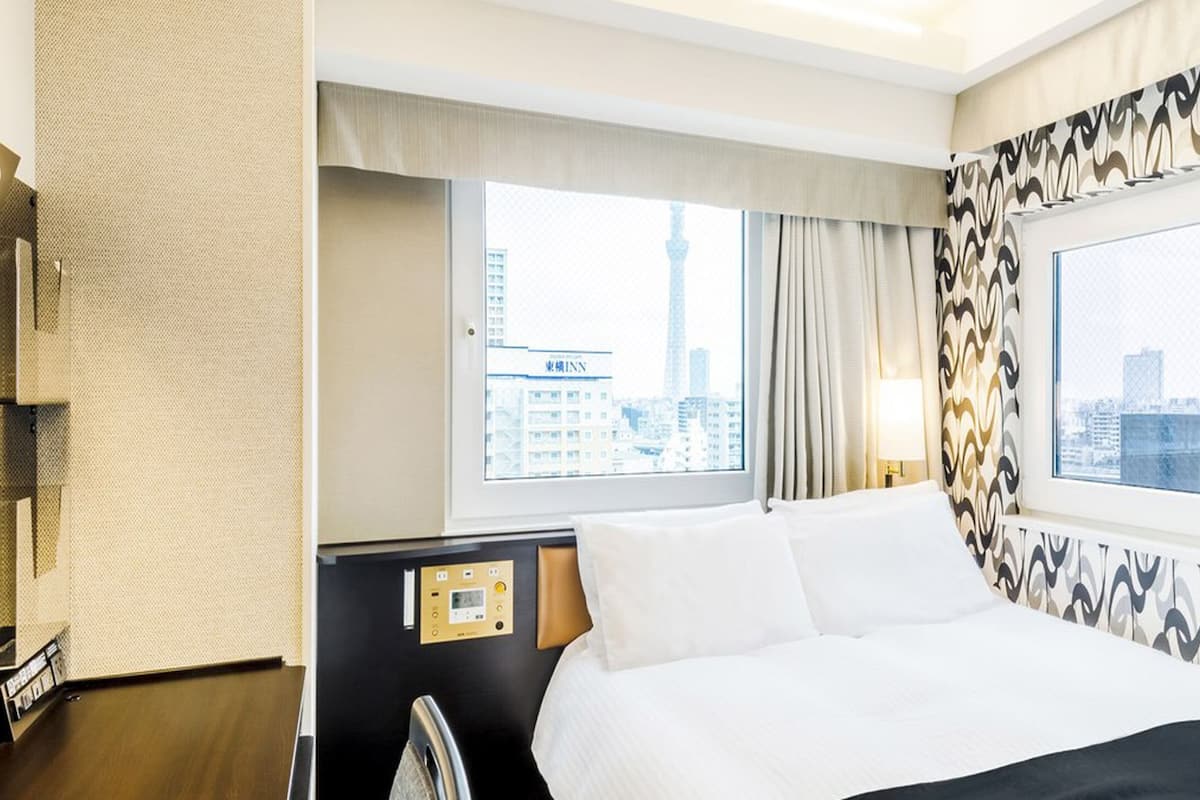 Una habitación de hotel con cama, panel de control, ventana con vista a la ciudad y cortinas estampadas.