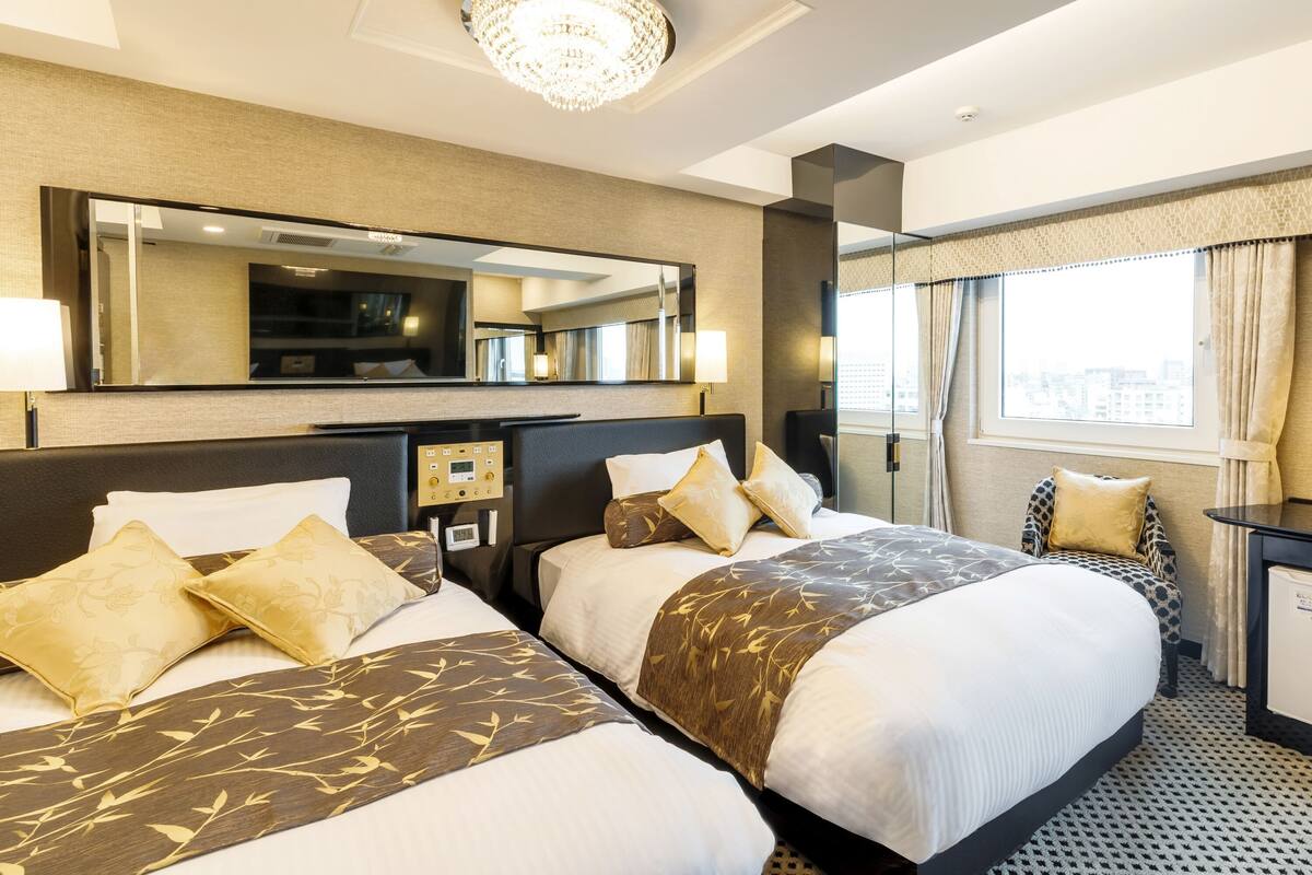 A hotel room with two beds, a large mirror, a television, and a window with curtains.