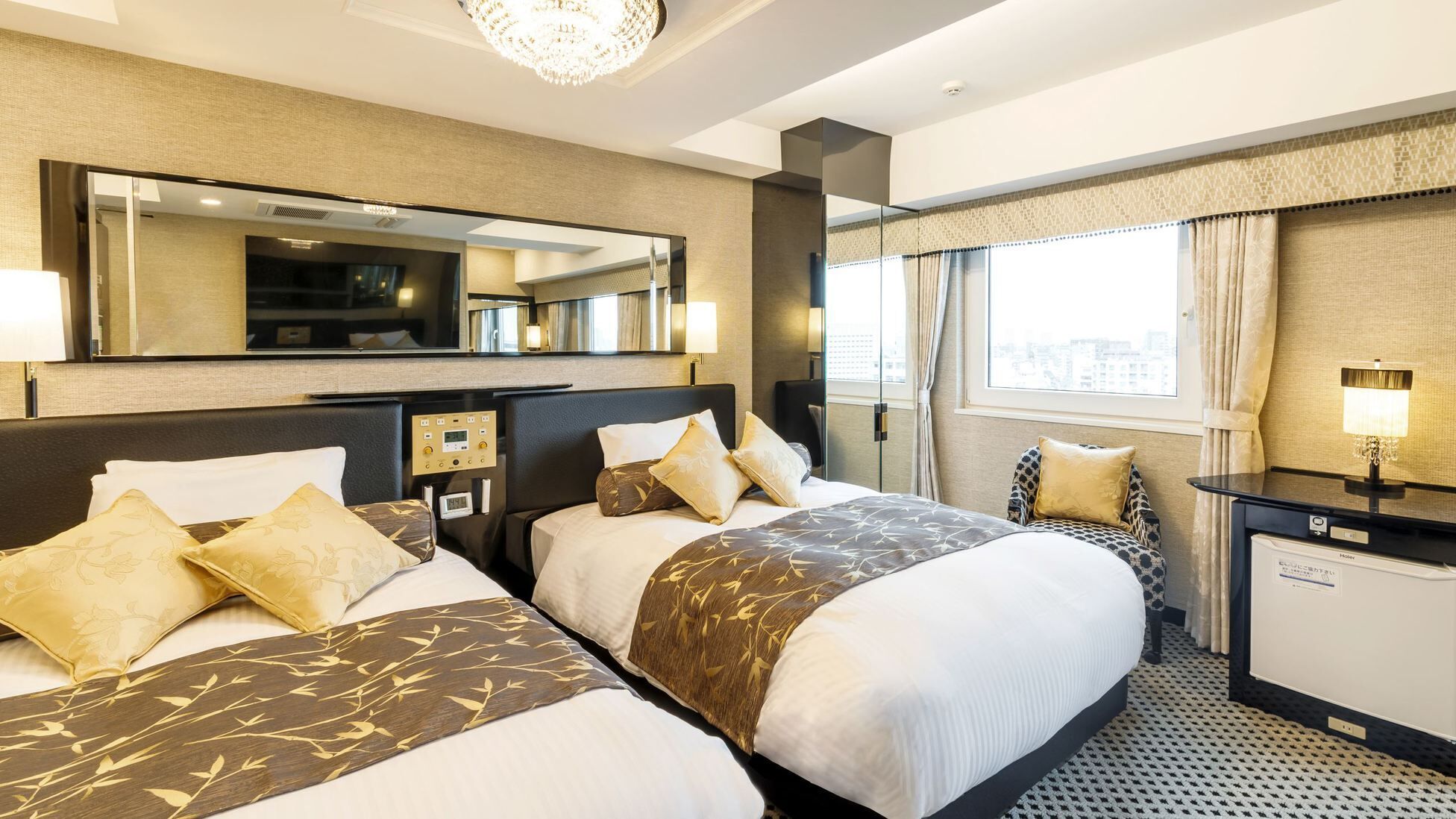 A hotel room with two beds, a TV, a desk, and a large window.