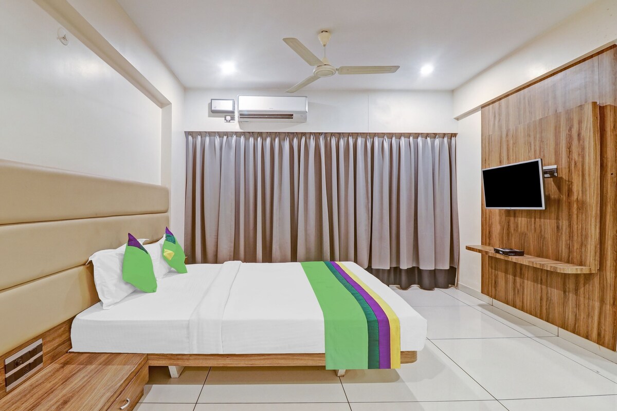 A modern hotel room with a bed, a ceiling fan, an air conditioning unit, a TV mounted on a wooden panel, and a wardrobe.
