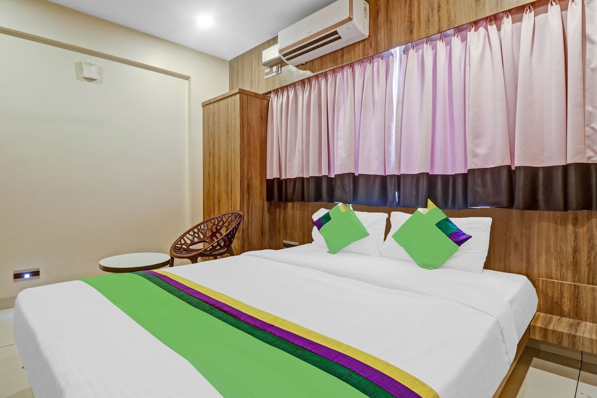 A hotel room with a bed, a chair, an air conditioning unit, and a window with curtains.