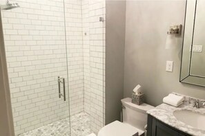 A bathroom with a glass-enclosed shower, white tiled walls, a marble sink, and a toilet. - Entire farmhouse in the country (Winterset)