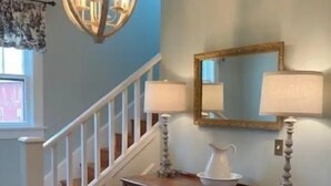 A staircase with white railings, a wooden floor, a wooden console table with a pitcher and lamps, and a chandelier. - Entire farmhouse in the country (Winterset)